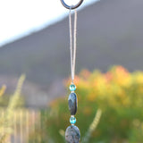 Top of azurite malachite stone sun catcher showing a 4&quot; loop of stainless steel wire covered in silver-lined seed beads, hanging from a hook. Below the loop are two stone beads and two small turquoise glass beads. A mountain slope and some foliage is in the background slightly blurred.