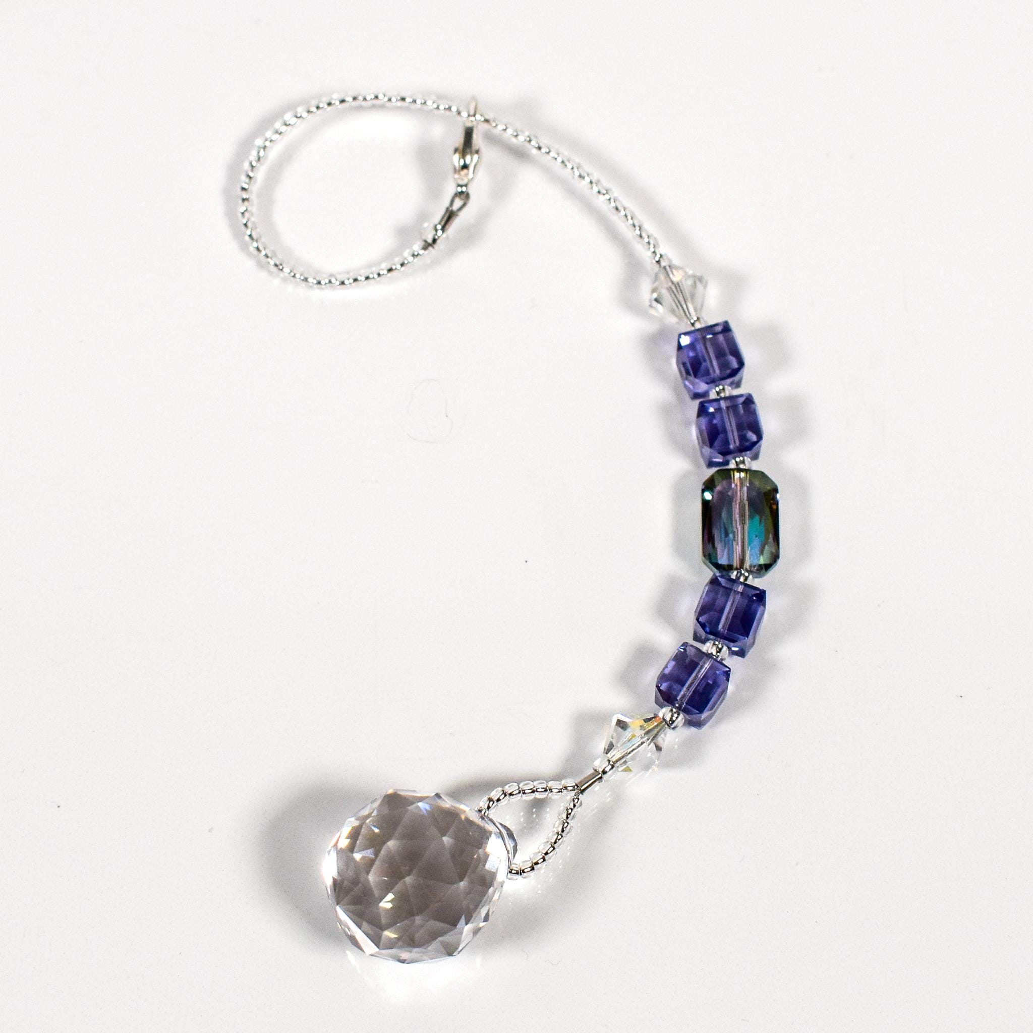 Small sun catcher coiled on a white surface, made with purple crystal cube beads, a large emerald cut crystal and a round crystal prism anchor.