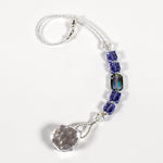 Small sun catcher coiled on a white surface, made with purple crystal cube beads, a large emerald cut crystal and a round crystal prism anchor.
