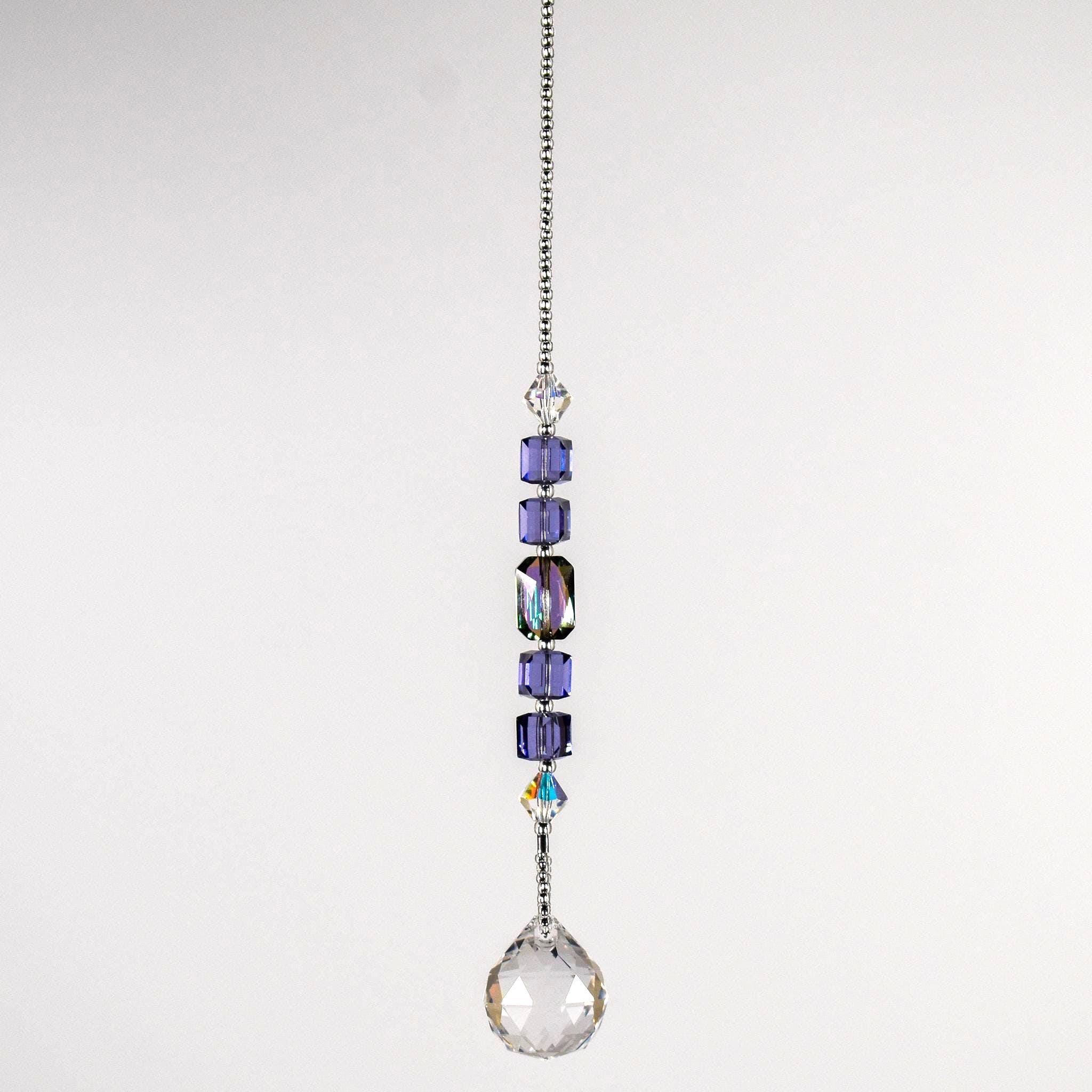 Small sun catcher hanging vertically against blurred background, made with purple crystal cube beads, a large emerald cut crystal and a round crystal prism anchor.