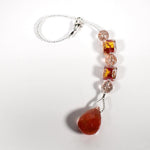 Small pink and gold sun catcher coiled on a white surface, made with Murano glass beads and a stone pendant.
