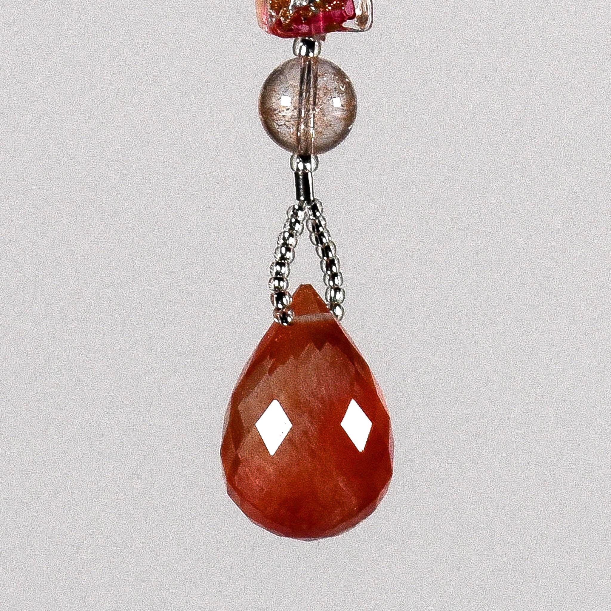 A teardrop shaped pink crystal pendant with a faceted design. The pendant is hanging from a wire covered in silver-lined seed beads. There is a pink crackle glass bead above the pendant.