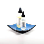 Square fused glass dish with solid blue center, black trim and black base, sitting white surface. Two bottles of skin care products are placed in the tray showing how it will work as a bathroom tray.