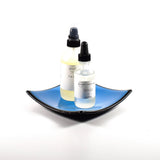 Square fused glass dish with solid blue center, black trim and black base, sitting white surface. Two bottles of skin care products are placed in the tray showing how it will work as a bathroom tray.