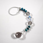 9 inch long sun catcher on a flat white surface, consisting of a single glass crystal cross bed with reflective finish, flanked by two large round glass crystal beads and six small rondelle-shaped turquoise beads, all anchored by a small glass crystal prism.