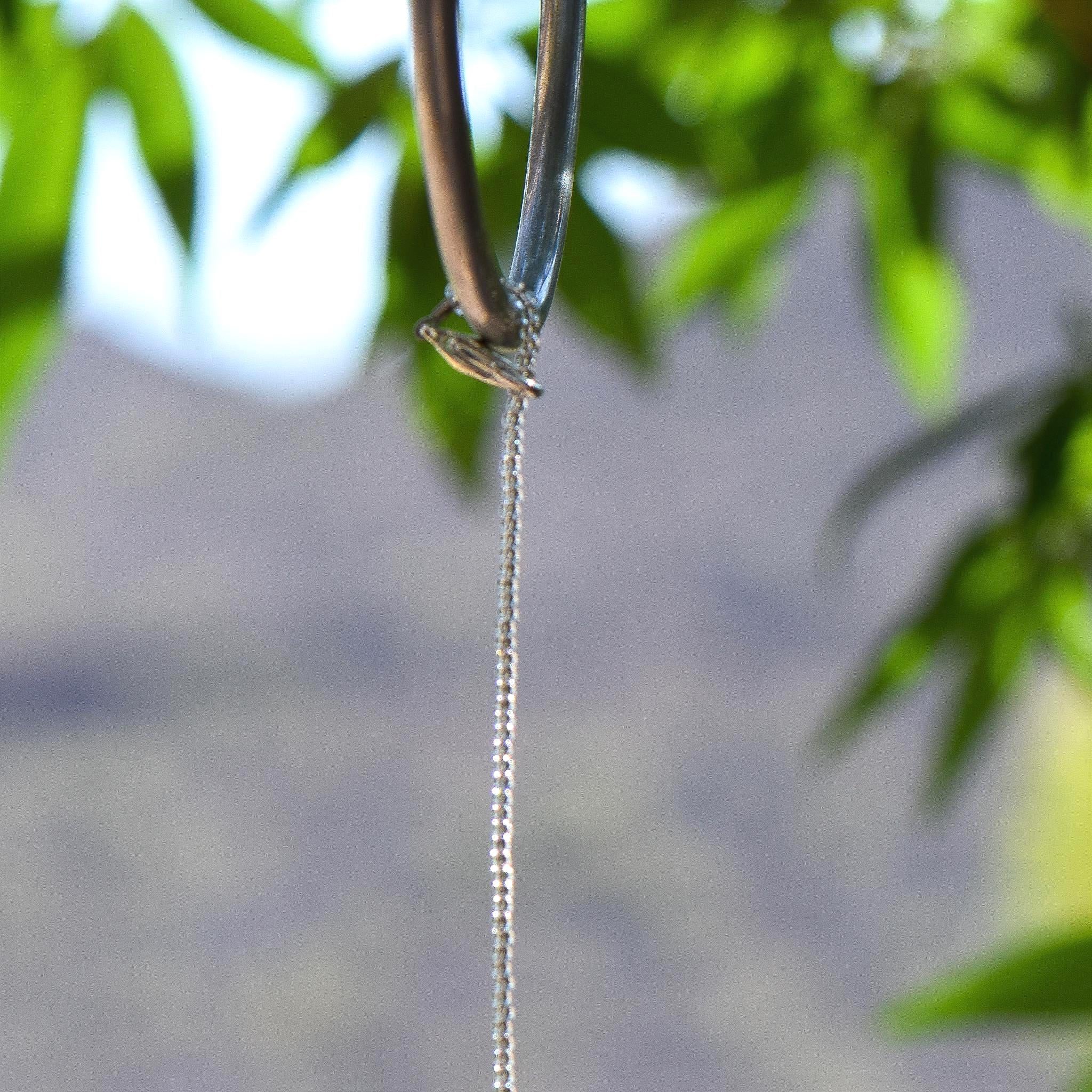 Close up view of the top of a typical small sun catcher from Cinjo Handmade showing stainless steel wire covered in silver-lined seed beads with a silver plated clasp at the top. The clasp is use to wrap the wire around a hook that is hanging from a tree.