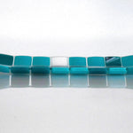 A rectangular glass tray with a mosaic tile design. The tray features a pattern of square tiles in shades of teal and white. The tiles are arranged in a grid-like pattern, creating a visually appealing surface. The tray is placed on a white surface. View is from the long side.