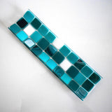 A rectangular glass tray with a mosaic tile design. The tray features a pattern of square tiles in shades of teal and white. The tiles are arranged in a grid-like pattern, creating a visually appealing surface. The tray is placed on a white surface. View is from the top.