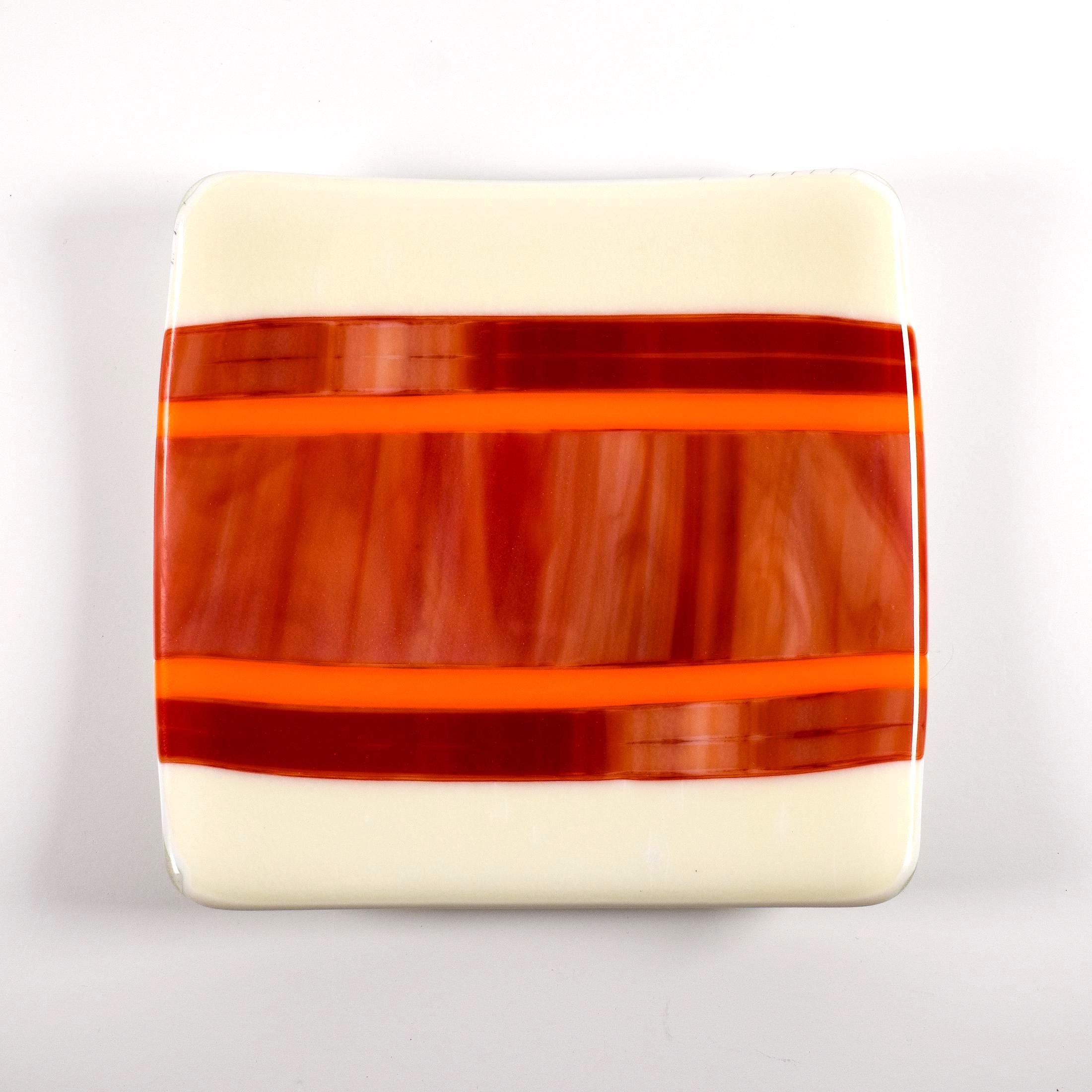 Square fused glass tray with vanilla cream colored base and a striped and streaky design of red, orange and white glass. Tray is 6&quot; square with upturned corners. Camera is looking straight down above the tray which is sitting on a white surface.