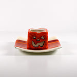 Square fused glass tray with vanilla cream colored base and a striped and streaky design of red, orange and white glass. A small pumpkin candle holder is sitting in the tray to show how it can be used. Tray is 6&quot; square with upturned corners. Sitting on a white surface.