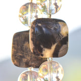 Two large silver leaf jasper stone beads, each flanked by large clear glass beads, hanging on wire with mountain in background.