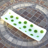 Channel-shaped rectangular fused glass tray in vanilla cream with green and yellow accents that look like lime slices. Placed diagonally on a stone table.