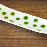 A white rectangular glass dish with a curved design. The dish is decorated with green accents. The patterns are evenly spaced across the surface. The dish is on a wooden surface.