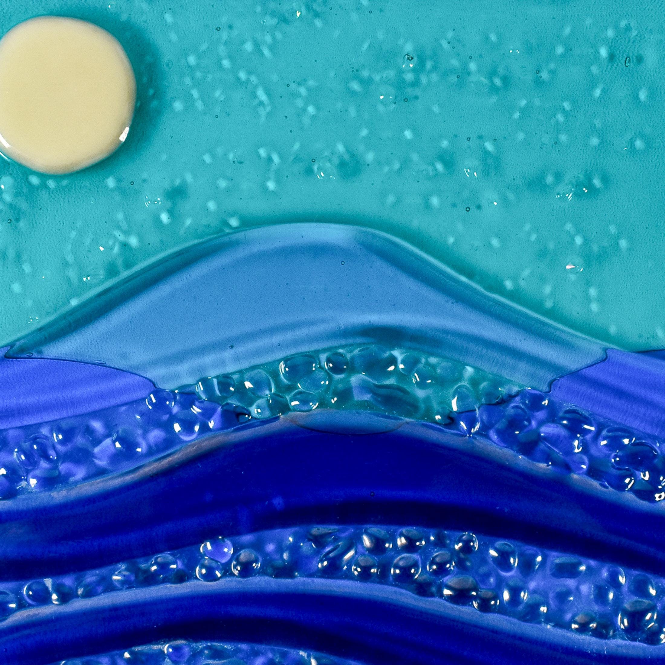 Close up of six inch square glass panel on a clear acrylic stand on a white background. The panel depicts waves of blue with texture and flow underneath a full moon in an evening sky.