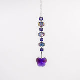 A handmade sun catcher featuring purple and iridescent crystal beads, finished with a faceted crystal butterfly pendant that reflects light in purple, blue, and gold tones. Suspended from a wire covered in silver-lined seed beads against a white background.