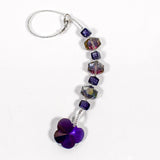 A handmade sun catcher featuring purple and iridescent crystal beads, finished with a faceted crystal butterfly pendant that reflects light in purple, blue, and gold tones. Curved, on a white surface.