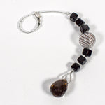Small sun catcher coiled on white surface, made with six Murano glass cube beads flanking a large, round swirly bead and anchored by a large smoky quartz pendant.