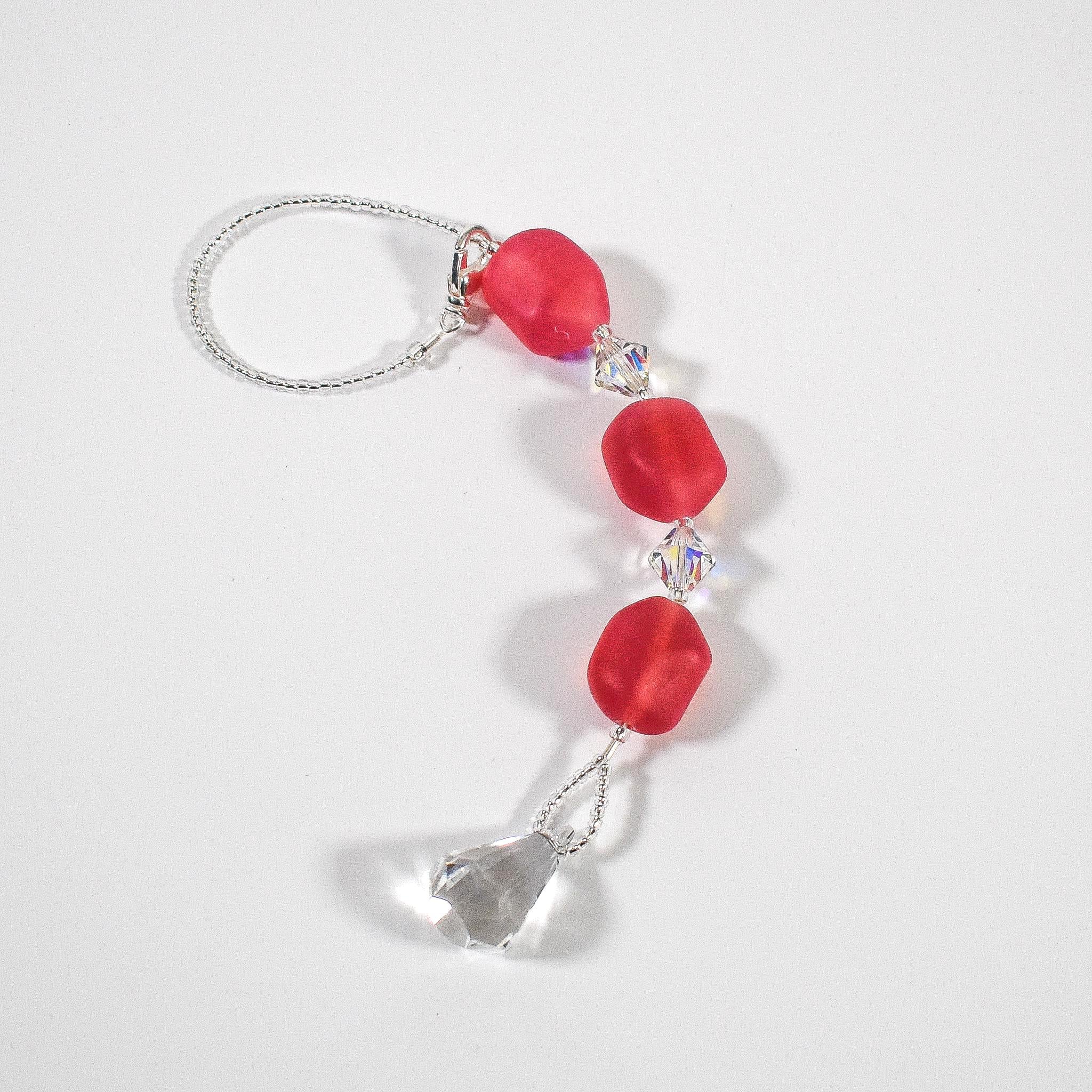 Pink beaded car rearview mirror charm coiled on white background.  The charm features three pink beads interspersed with clear crystal accents and a dangling clear crystal teardrop. The beads are irregular in shape and made of glass.  White background.