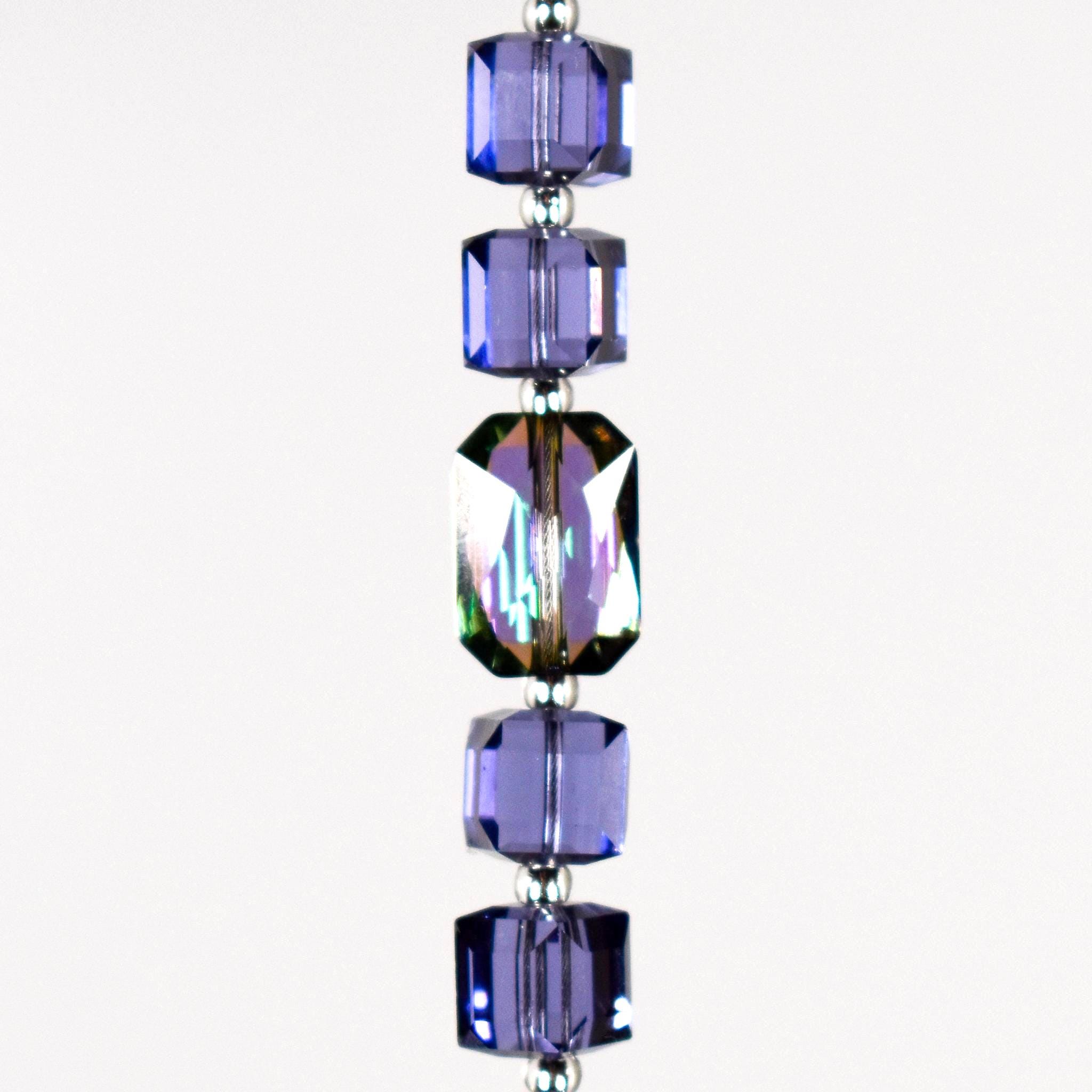 A strand of iridescent purple crystal beads with a clear crystal bead in the center. White background.