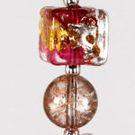 Close up view of cubic Murano glass bead in peach color with gold foil above a pink crackle glass bead.