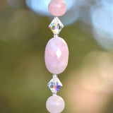 Close-up of a oval-shaped rose quartz stone beads, strung with smaller rose quartz beads and glass crystal bicone beads.