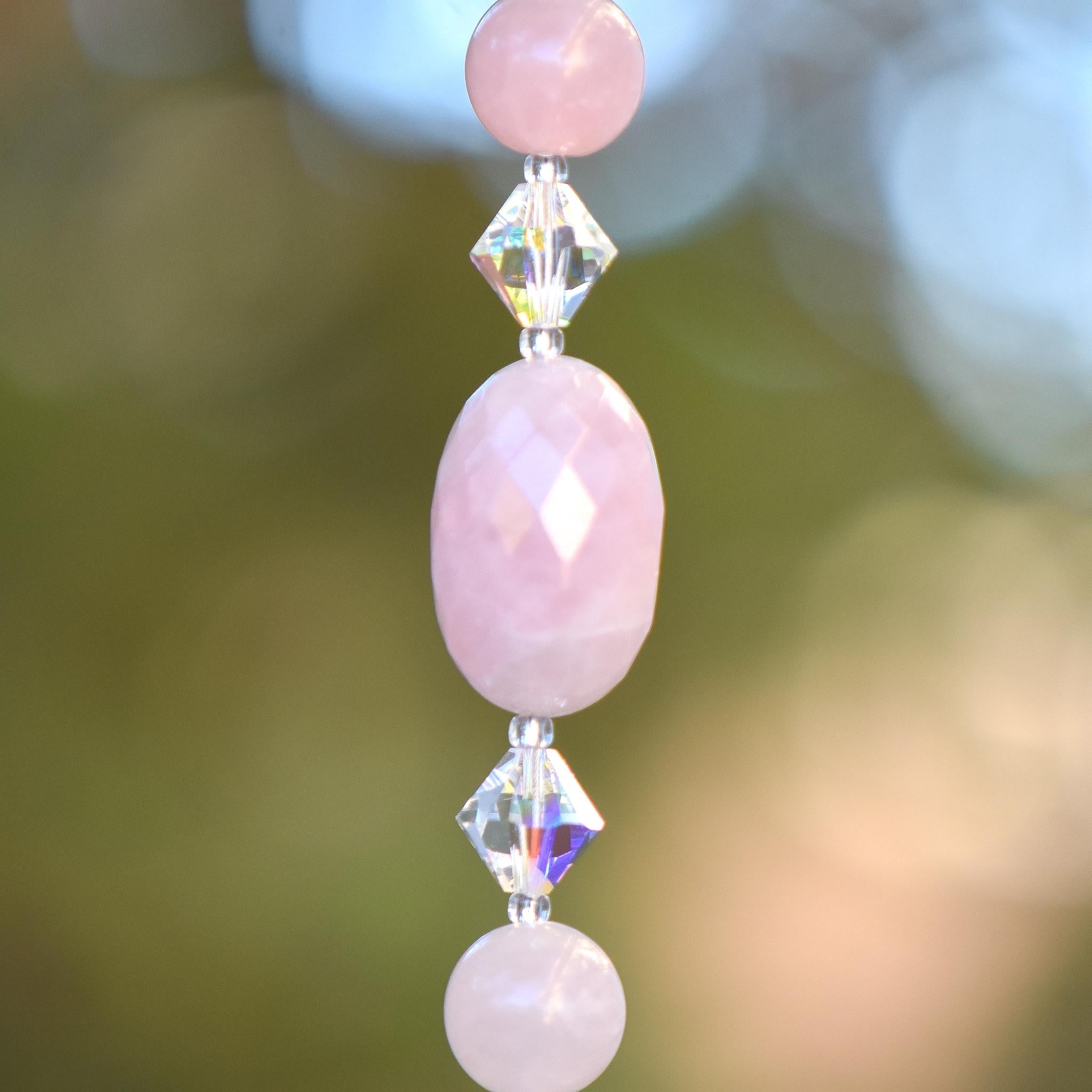 Close-up of a oval-shaped rose quartz stone beads, strung with smaller rose quartz beads and glass crystal bicone beads.