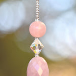 Large oval rose quartz bead flanked by Austrian crystal and two smaller round rose quartz beads, hanging vertically from a tree, anchored by round crystal prism.
