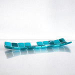 A rectangular glass tray with a mosaic tile design. The tray features a pattern of square tiles in shades of teal and white. The tiles are arranged in a grid-like pattern, creating a visually appealing surface. The tray is placed on a white surface.