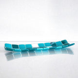 A rectangular glass tray with a mosaic tile design. The tray features a pattern of square tiles in shades of teal and white. The tiles are arranged in a grid-like pattern, creating a visually appealing surface. The tray is placed on a white surface.