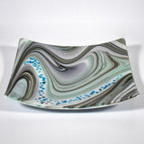 Large 12&quot; glass tray on white surface, viewed from above at an angle. Tray is white with swirl pattern in gray, tan and aqua, embellished with flecks of cream and aqua glass. Display as art or use as centerpiece or serving tray.