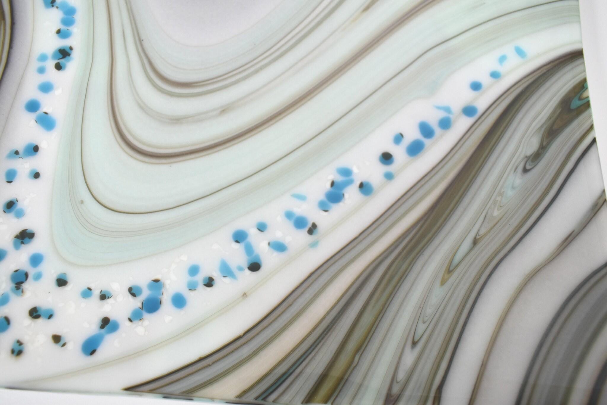 Close-up of a white, blue, and brown marbled surface with blue and black flecks. The surface has a wavy pattern.