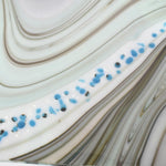 Close-up of a white, blue, and brown marbled surface with blue and black flecks. The surface has a wavy pattern.