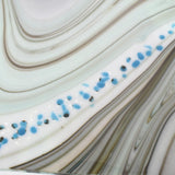 Close-up of a white, blue, and brown marbled surface with blue and black flecks. The surface has a wavy pattern.