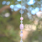 Large oval rose quartz bead flanked by Austrian crystal and two smaller round rose quartz beads, hanging vertically from a tree, anchored by round crystal prism.