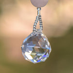 Close-up of a crystal pendant featuring a faceted, clear crystal ball hanging from a bead-covered stainless steel wire. The crystal displays rainbow-like iridescence.