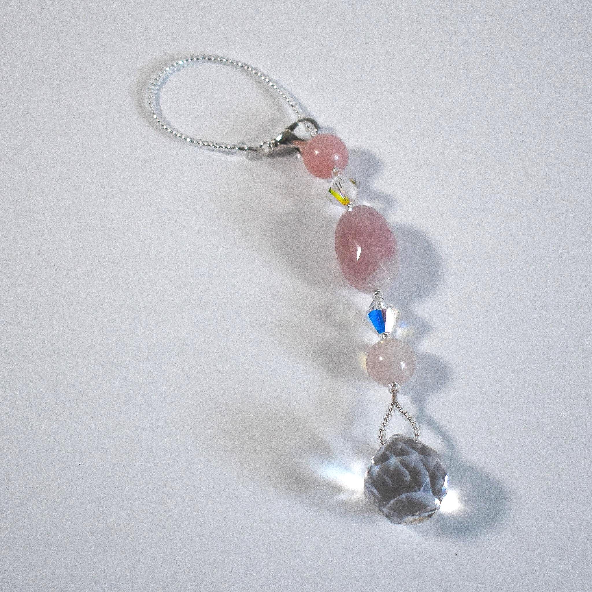 Large oval rose quartz bead flanked by Austrian crystal and two smaller round rose quartz beads, placed on a white background.