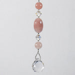 Large oval rose quartz bead flanked by Austrian crystal and two smaller round rose quartz beads, hanging vertically against a white background.