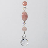 Large oval rose quartz bead flanked by Austrian crystal and two smaller round rose quartz beads, hanging vertically against a white background.