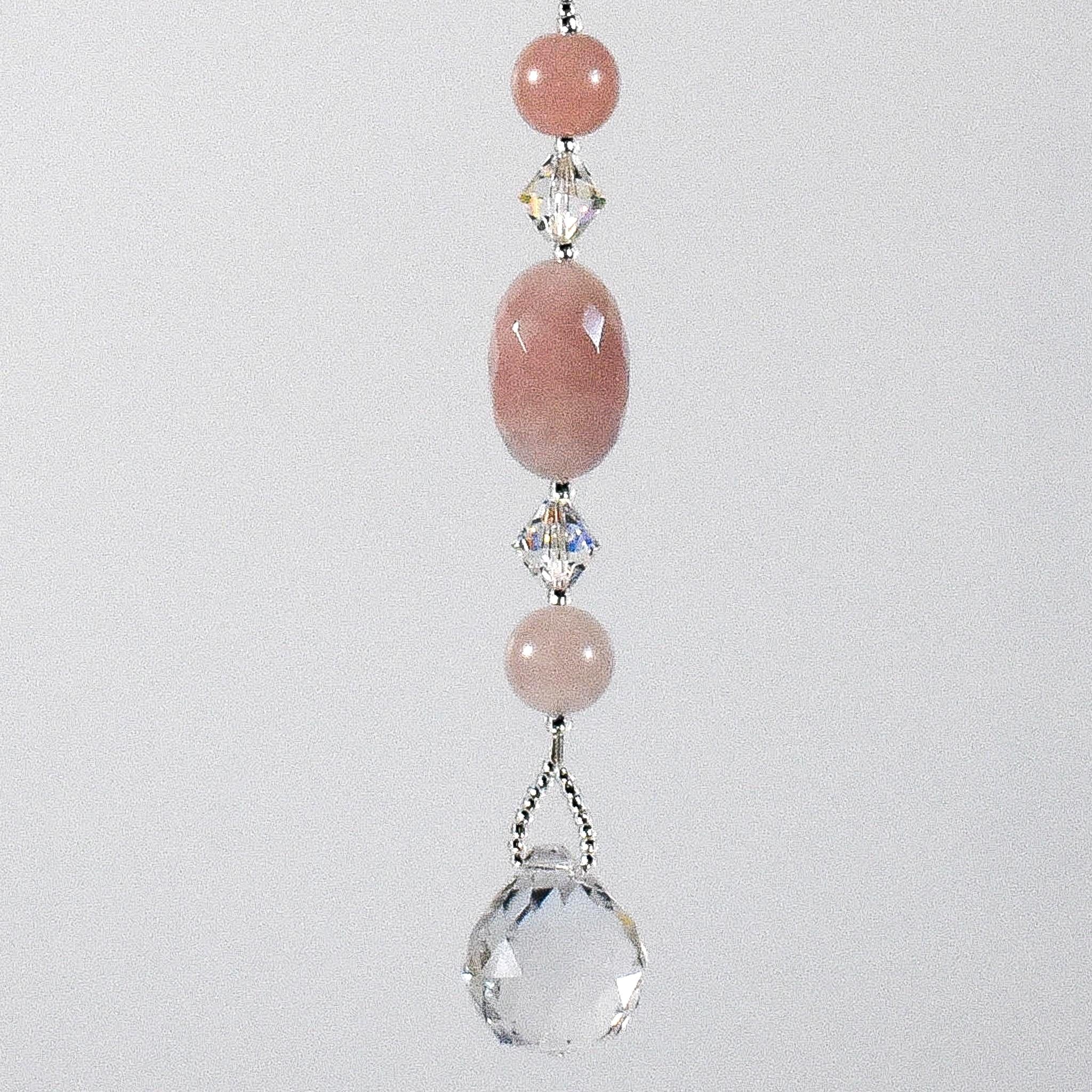 Large oval rose quartz bead flanked by Austrian crystal and two smaller round rose quartz beads, hanging vertically against a white background.