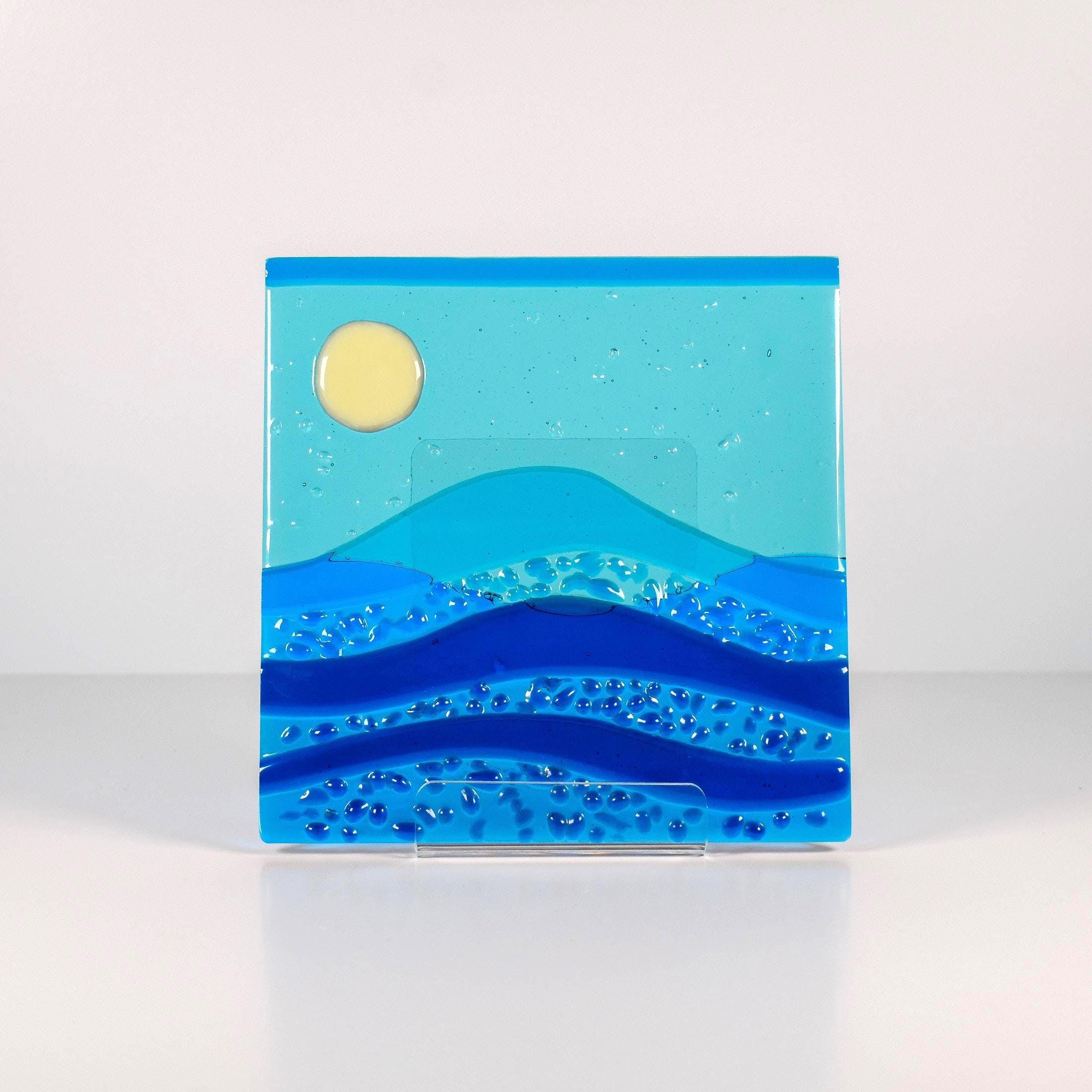 Six inch square glass panel on a clear acrylic stand on a white background. The panel depicts waves of blue with texture and flow underneath a full moon in an evening sky.