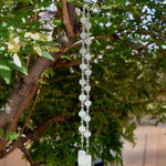 Cinjo Handmade wind chime hanging from a tree in suburban setting. Two legs of large sea glass beads are pictured, strung with smaller clear glass beads and anchored by two pieces of kiln formed glass.