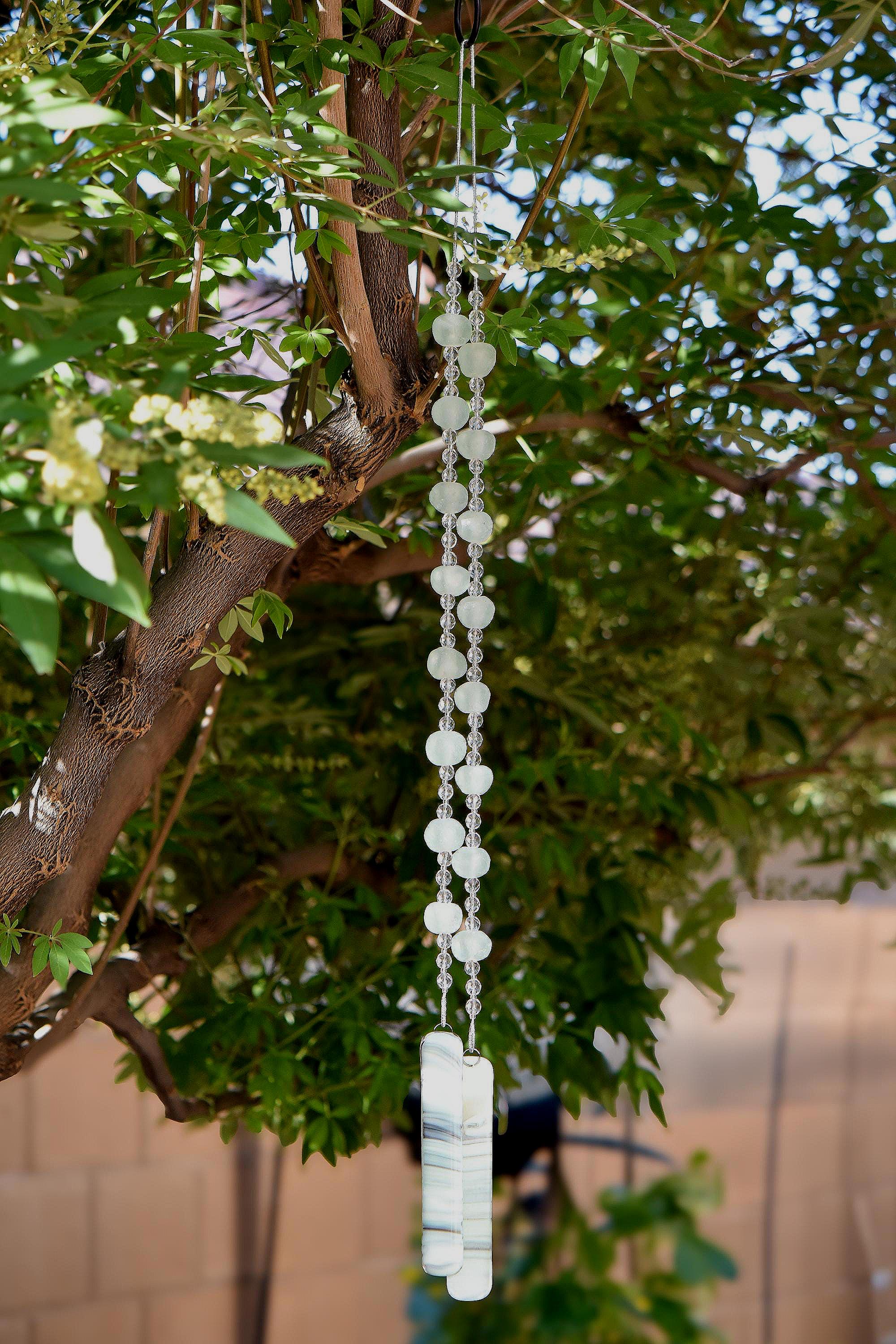 Cinjo Handmade wind chime hanging from a tree in suburban setting. Two legs of large sea glass beads are pictured, strung with smaller clear glass beads and anchored by two pieces of kiln formed glass.