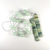 Cinjo Handmade wind chime coiled on a white surface. Large sea glass beads are pictured, strung with smaller clear glass beads and anchored by two pieces of kiln formed glass.