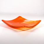Fused glass tray made of clear glass with streaks of bright orange viewed from the side showing upturned corners. Background is white.