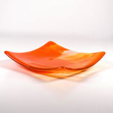 Fused glass tray made of clear glass with streaks of bright orange viewed from the side showing upturned corners. Background is white.