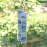 Two pieces of streaky fused glass hanging vertically from a tree. The glass has a cream background and streaks of black, gray and tan with a slight bluish/green hue. Each piece is rectangular. At the top of each glass piece are small faceted glass crystal beads.