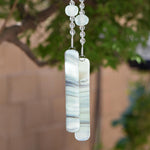 Bottom of hanging wind chime from Cinjo Handmade.Four large sea glass beads are pictured, strung with smaller clear glass beads and anchored by two pieces of kiln formed glass. The chime is hanging in front of blurred foliage.