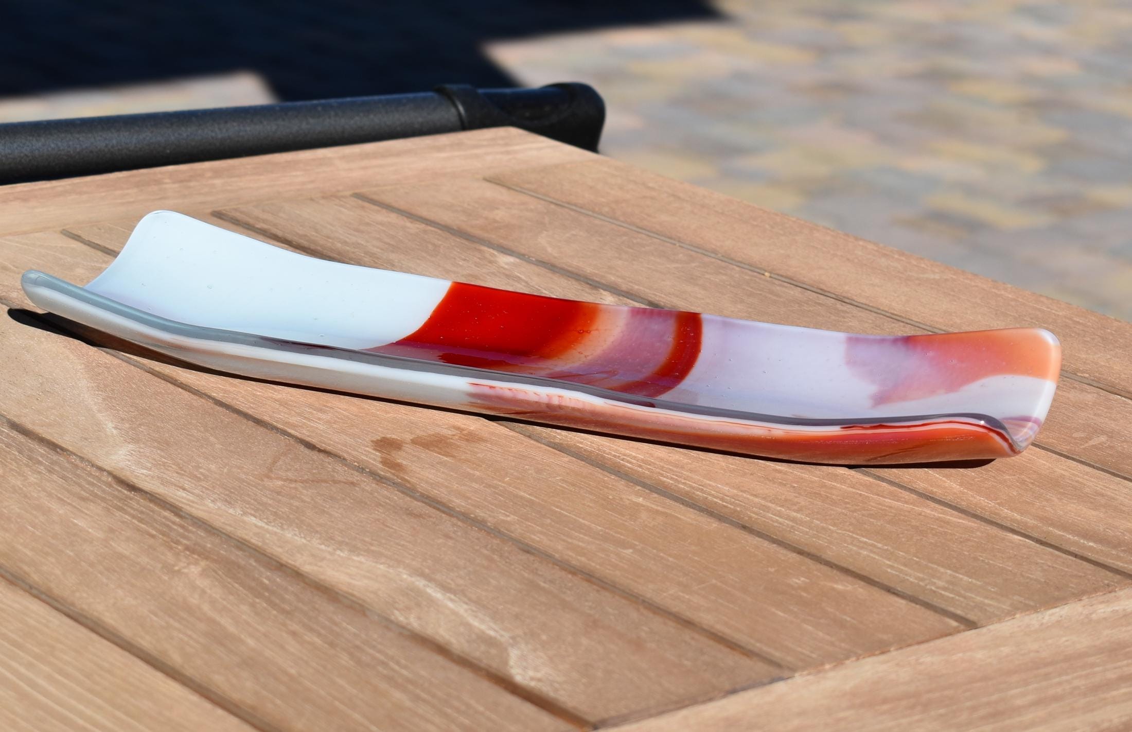 Long fused glass channel tray outdoors on a wood table, white with red, orange and pink design.