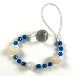 Long sun catcher from Cinjo Handmade coiled on white surface. Sun catcher has a 4 inch loop at the top and includes 3 large round beads made of white quartz. Two of these quartz beads are more off white or cream colored. There are 3 smaller deep aqua blue round glass beads between each of the quartz beads. A round glass crystal prism anchors the piece.