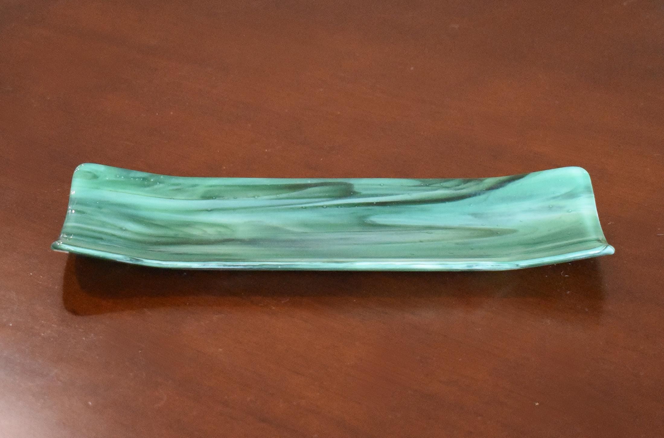 Green and seafoam fused glass channel tray on a brown tabletop, showing marbled swirls and subtle bubbles.